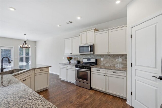 kitchen with dark wood finished floors, visible vents, decorative backsplash, stainless steel appliances, and a sink