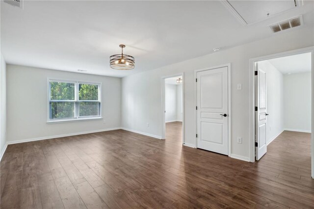 unfurnished room with dark wood-type flooring, attic access, baseboards, and visible vents