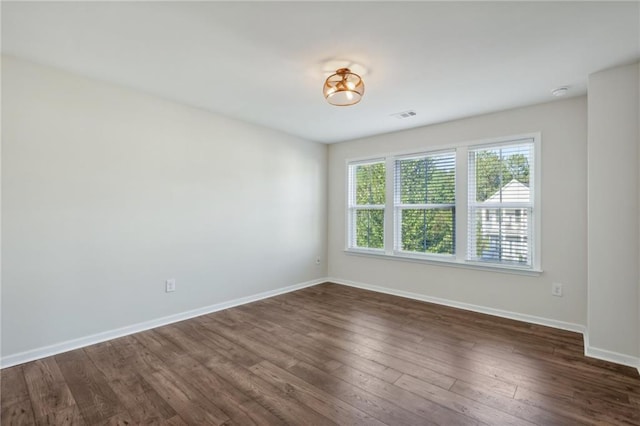 unfurnished room with dark wood-type flooring, visible vents, and baseboards