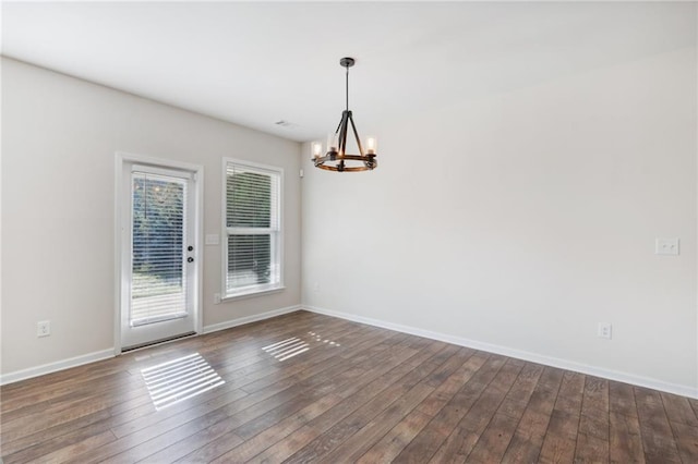unfurnished room featuring baseboards, an inviting chandelier, and dark wood finished floors