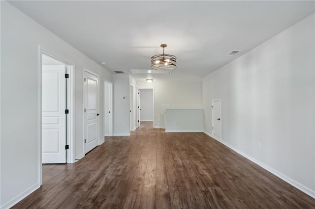 unfurnished living room featuring attic access, dark wood-style flooring, baseboards, and visible vents