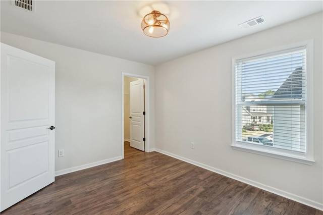 unfurnished bedroom with dark wood-style flooring, visible vents, and baseboards