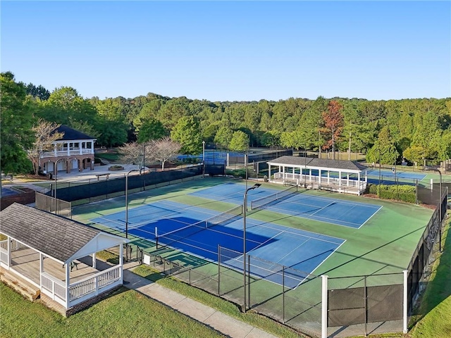 view of tennis court featuring a wooded view and fence
