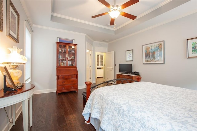 bedroom with dark wood-style floors, a tray ceiling, baseboards, and crown molding