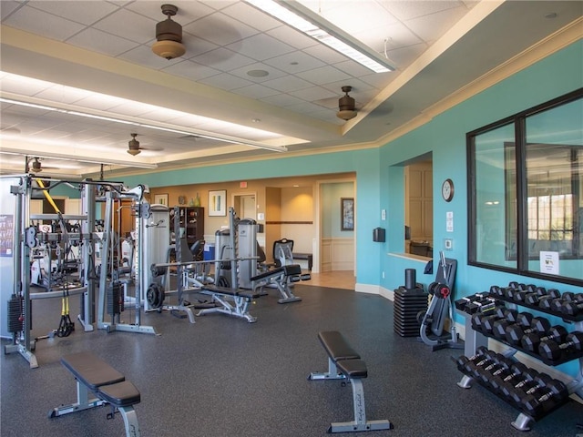 gym featuring ceiling fan, a drop ceiling, baseboards, a raised ceiling, and crown molding