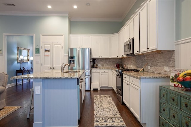 kitchen with stainless steel appliances, white cabinets, ornamental molding, and light stone countertops