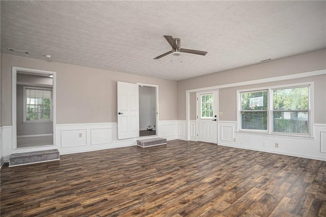 unfurnished room with dark wood finished floors, a textured ceiling, a ceiling fan, a wainscoted wall, and a decorative wall