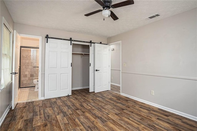 unfurnished bedroom with dark wood-type flooring, a textured ceiling, baseboards, a barn door, and connected bathroom