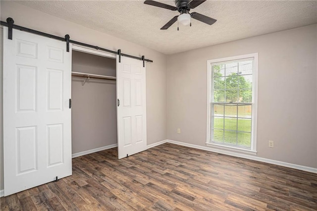 unfurnished bedroom featuring a barn door, dark wood-type flooring, a textured ceiling, and baseboards