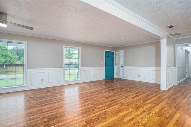unfurnished room with a textured ceiling, light wood-type flooring, plenty of natural light, crown molding, and a wainscoted wall