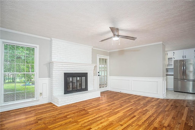 unfurnished living room featuring light wood-style flooring, ceiling fan, a textured ceiling, a fireplace, and ornamental molding