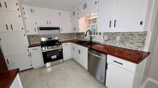 kitchen with stainless steel appliances, a sink, exhaust hood, white cabinetry, and a textured ceiling