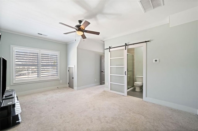 unfurnished bedroom with light colored carpet, ensuite bath, a barn door, ornamental molding, and ceiling fan