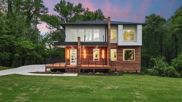 back house at dusk with a wooden deck and a lawn