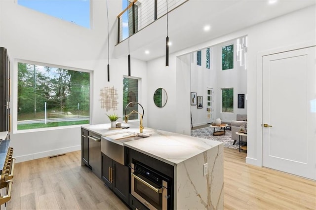 kitchen featuring light stone countertops, sink, hanging light fixtures, an island with sink, and light hardwood / wood-style floors