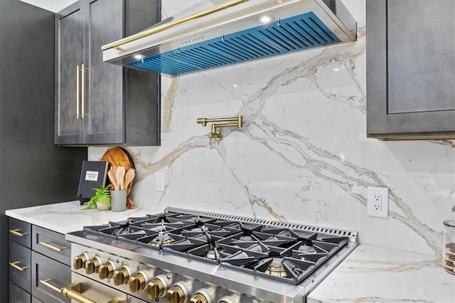 kitchen with decorative backsplash, light stone countertops, range, and exhaust hood