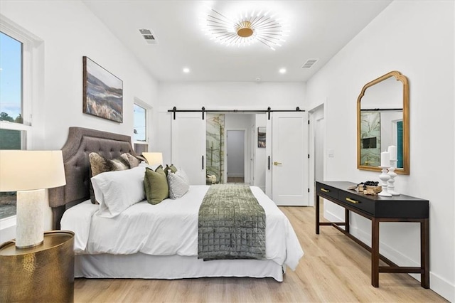 bedroom with a barn door and light hardwood / wood-style flooring