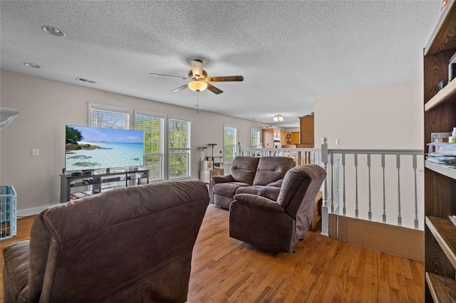 living room with ceiling fan, light hardwood / wood-style floors, and a textured ceiling