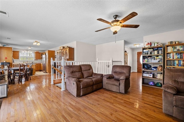 living room with ceiling fan, a textured ceiling, and light hardwood / wood-style floors