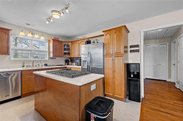 kitchen with sink, a center island, a textured ceiling, and appliances with stainless steel finishes