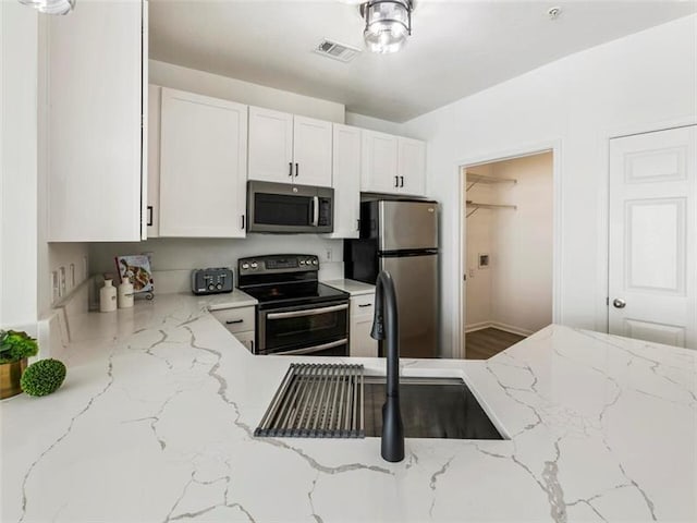 kitchen featuring white cabinetry, sink, light stone counters, and appliances with stainless steel finishes