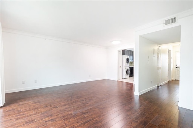 unfurnished room featuring dark hardwood / wood-style flooring, stacked washer and dryer, and ornamental molding