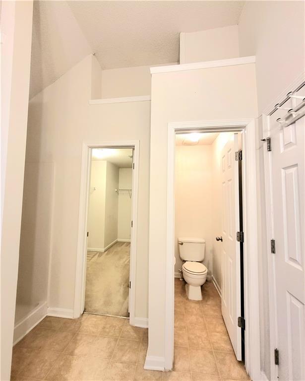 bathroom with lofted ceiling, tile patterned flooring, toilet, and baseboards