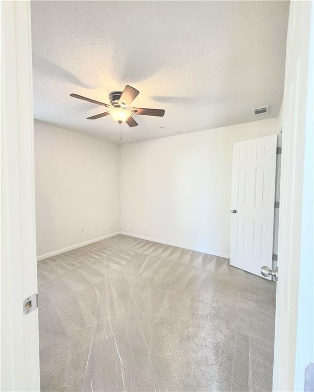 empty room featuring baseboards, visible vents, a ceiling fan, light colored carpet, and a textured ceiling