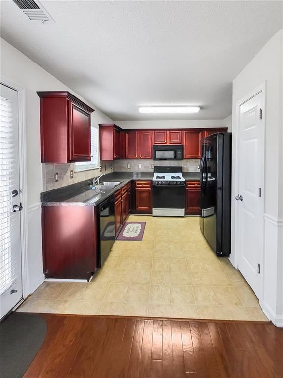 kitchen with visible vents, backsplash, reddish brown cabinets, black appliances, and dark countertops