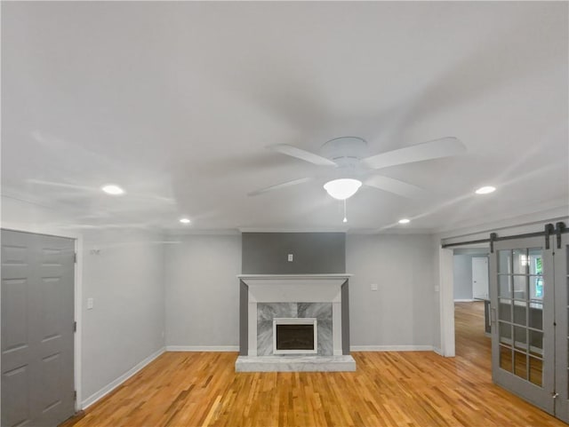 unfurnished living room with light hardwood / wood-style flooring, a fireplace, a barn door, and ceiling fan