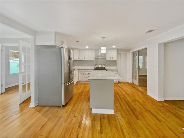 kitchen featuring pendant lighting, wall chimney range hood, appliances with stainless steel finishes, white cabinetry, and a kitchen island