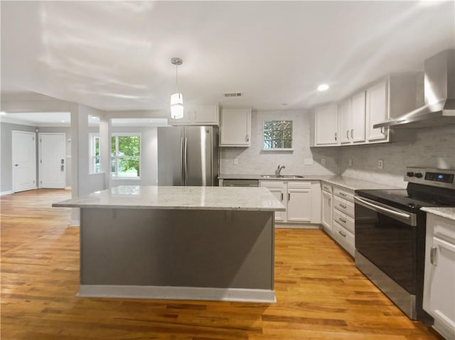 kitchen featuring stainless steel appliances, a center island, white cabinets, decorative light fixtures, and wall chimney exhaust hood