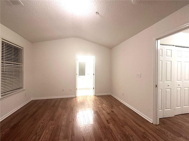 spare room with vaulted ceiling, a textured ceiling, and dark hardwood / wood-style flooring