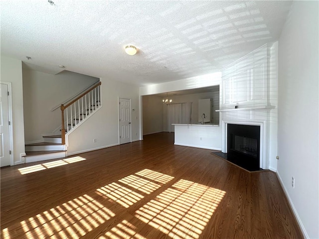 unfurnished living room featuring sink, dark wood-type flooring, an inviting chandelier, a large fireplace, and a textured ceiling