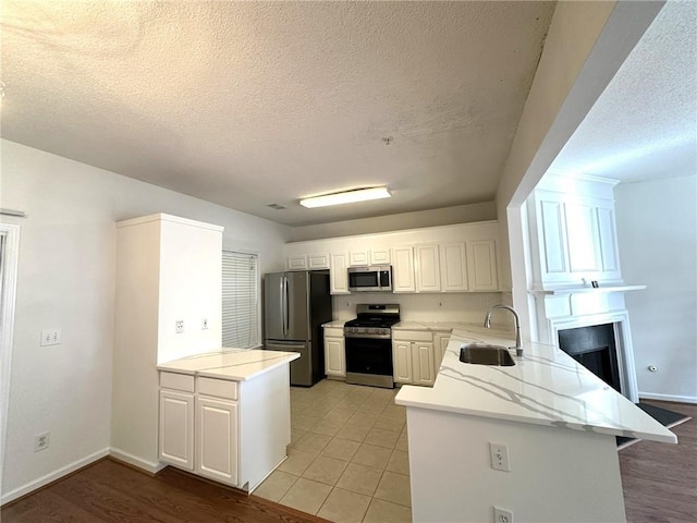 kitchen with sink, stainless steel appliances, a textured ceiling, white cabinets, and kitchen peninsula