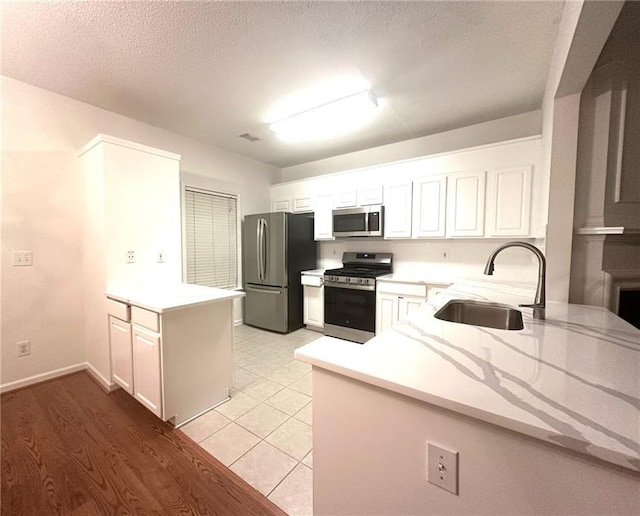 kitchen featuring sink, appliances with stainless steel finishes, a textured ceiling, white cabinets, and kitchen peninsula