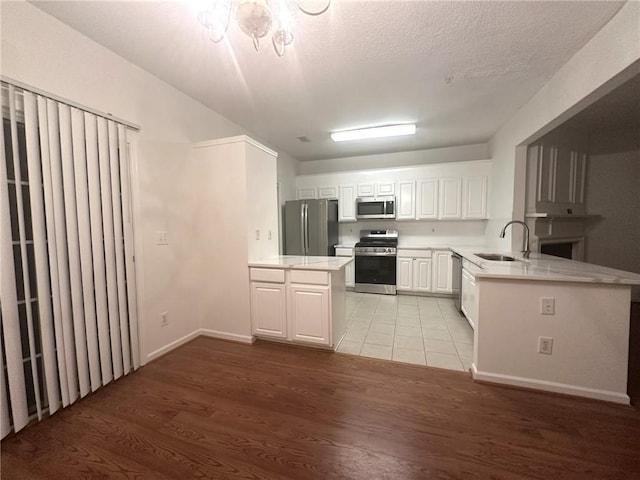 kitchen with appliances with stainless steel finishes, white cabinetry, sink, kitchen peninsula, and light hardwood / wood-style flooring