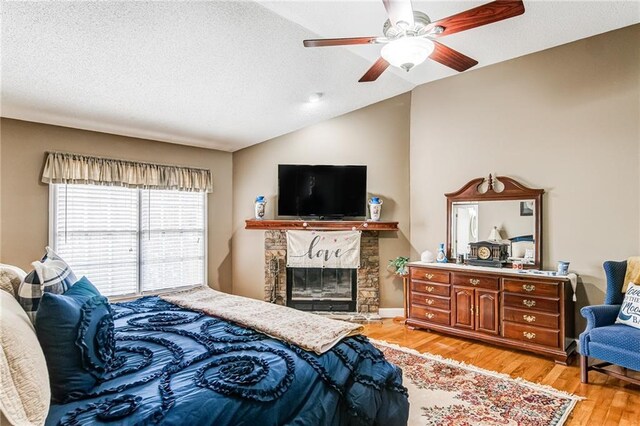 bedroom featuring light hardwood / wood-style floors, ceiling fan, a fireplace, a textured ceiling, and vaulted ceiling