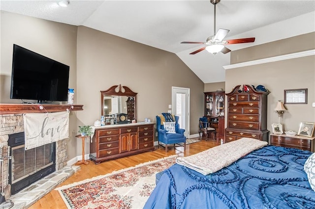 bedroom featuring a stone fireplace, ceiling fan, vaulted ceiling, and light wood-type flooring