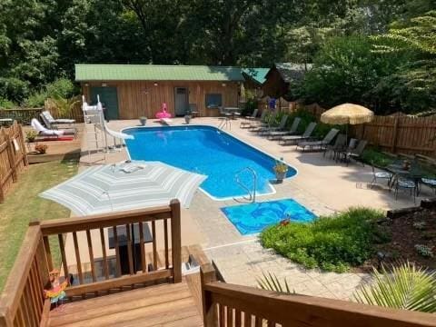 view of swimming pool featuring a deck, a water slide, a patio area, and an outdoor structure