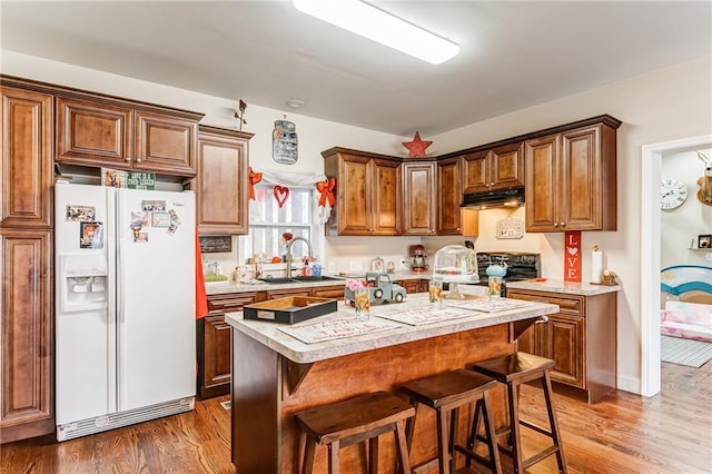 kitchen with a kitchen breakfast bar, a kitchen island, wood-type flooring, and white refrigerator with ice dispenser