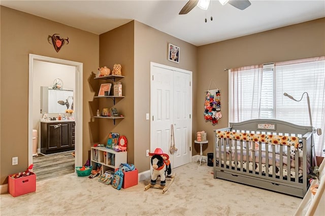 carpeted bedroom featuring a nursery area, connected bathroom, a closet, and ceiling fan