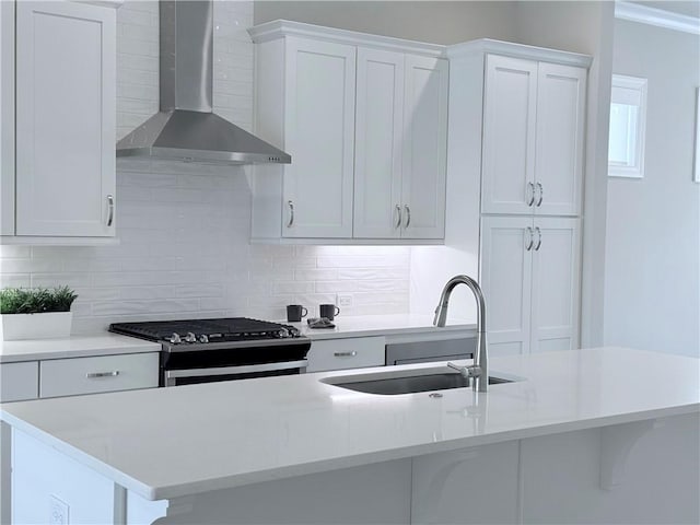 kitchen with gas stove, a sink, backsplash, and wall chimney range hood