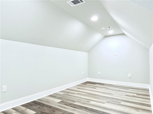 additional living space with vaulted ceiling, light wood-style floors, visible vents, and baseboards