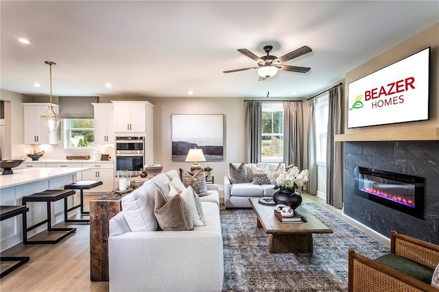 living room featuring ceiling fan, a tile fireplace, and light hardwood / wood-style floors