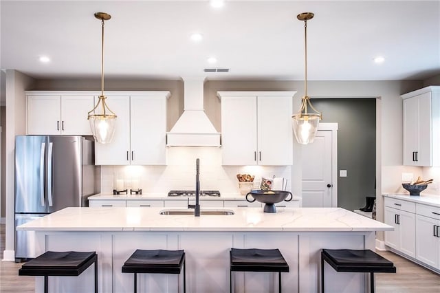 kitchen with custom exhaust hood, light stone counters, a kitchen island with sink, and stainless steel appliances