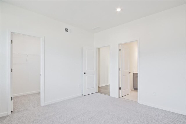 unfurnished bedroom featuring a spacious closet, ensuite bathroom, a closet, and light carpet