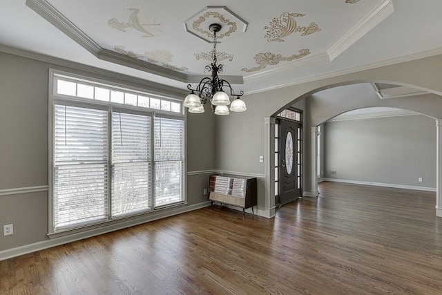 empty room featuring crown molding, a tray ceiling, dark hardwood / wood-style floors, and a chandelier