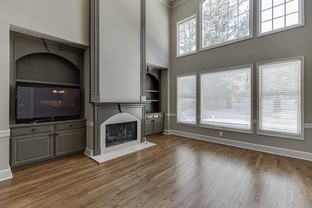 unfurnished living room with dark hardwood / wood-style floors, built in features, a high ceiling, a high end fireplace, and crown molding