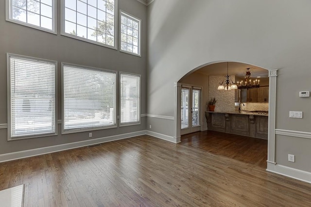 unfurnished living room with an inviting chandelier, dark hardwood / wood-style floors, sink, and a high ceiling